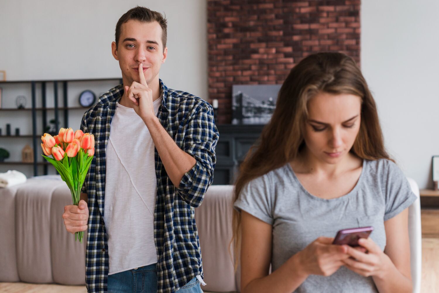 A man holding a bouquet of tulips with a finger to his lips while a woman in the foreground looks at her phone.