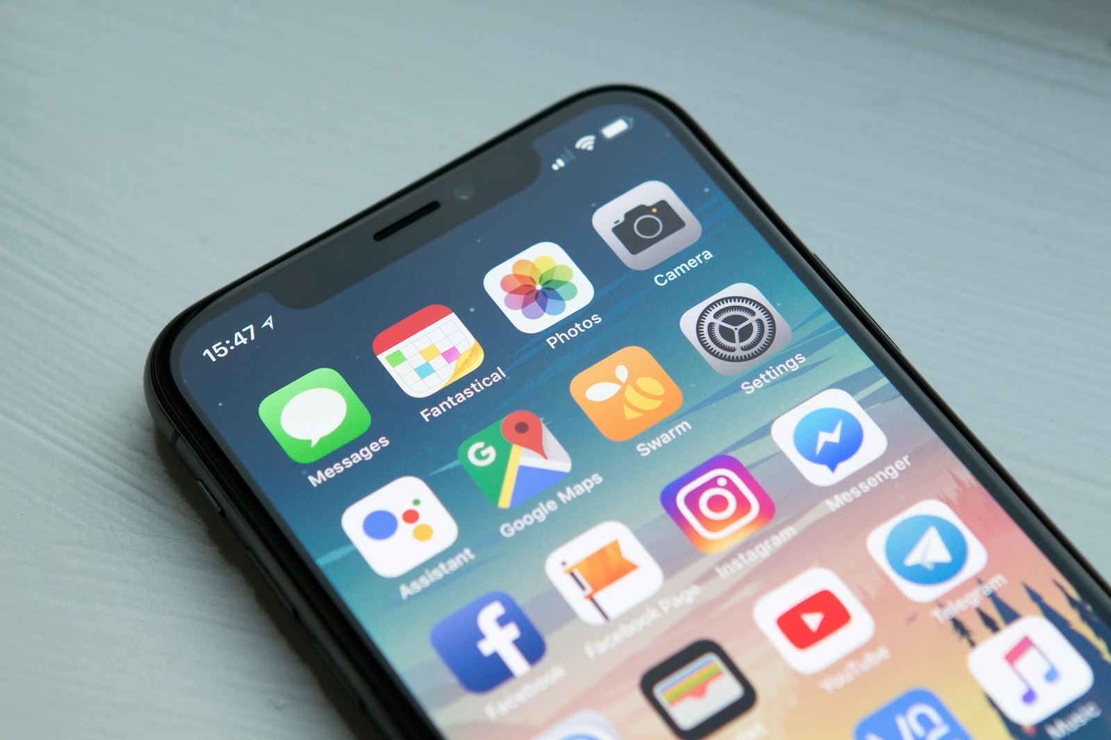 A close up of a smartphone home screen with apps wiggling, finger hovering over a delete X in soft daylight.