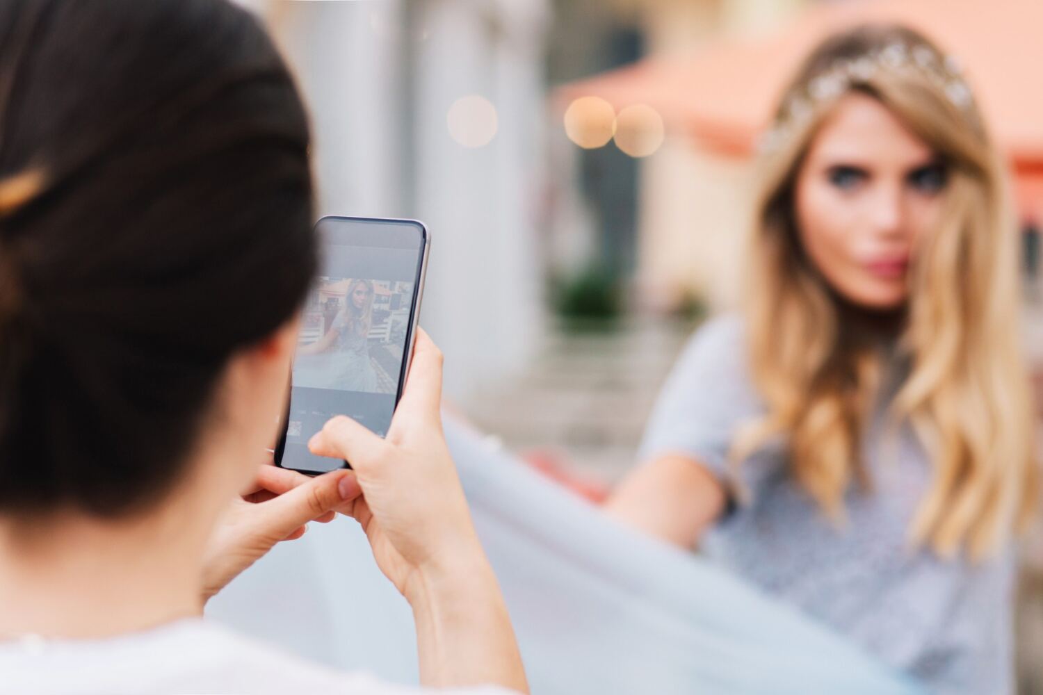 A person taking a phone photo of a blonde woman with a tiara outdoors.