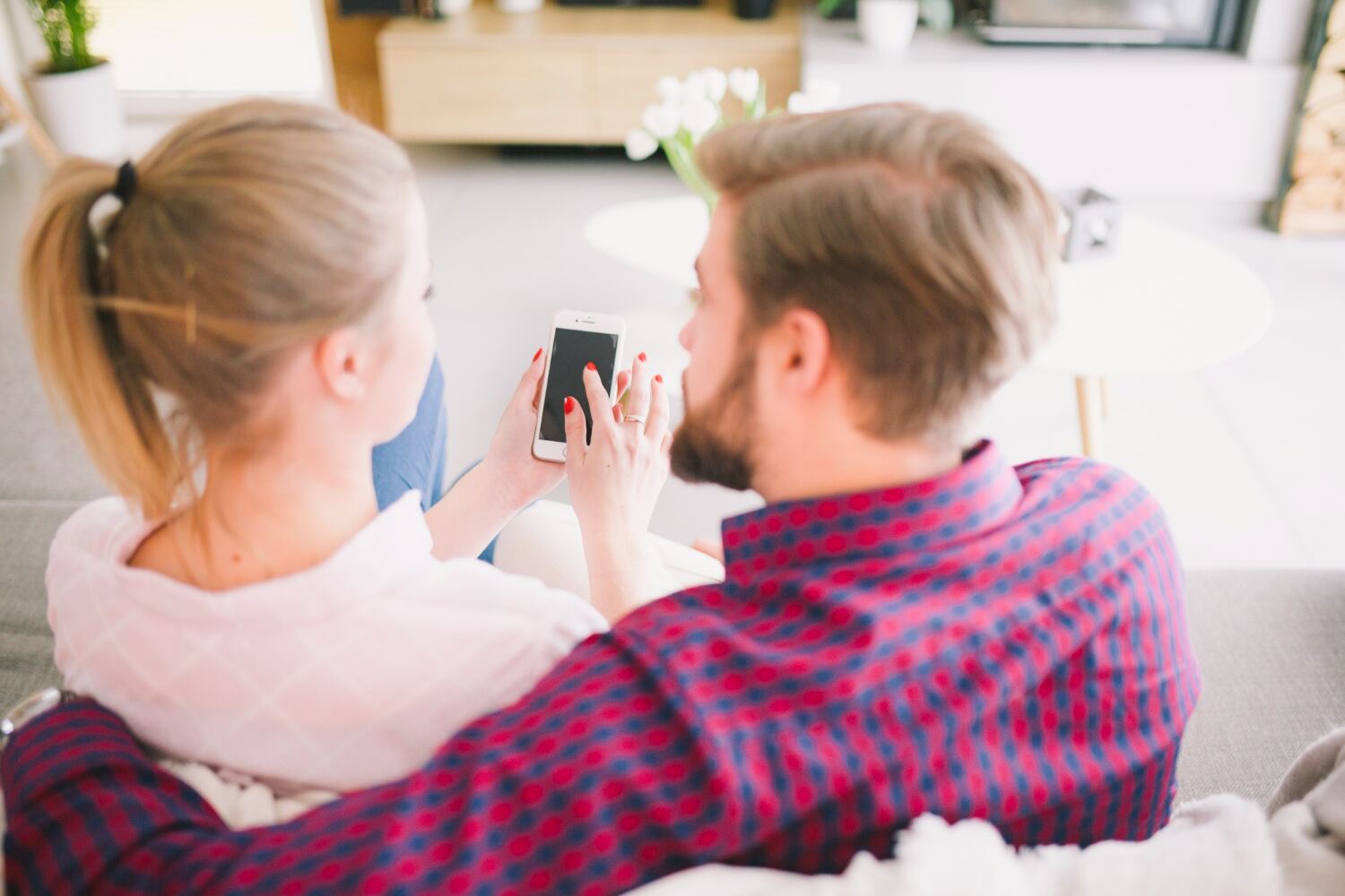 A couple sitting on a couch looking at a phone together in a bright living room.