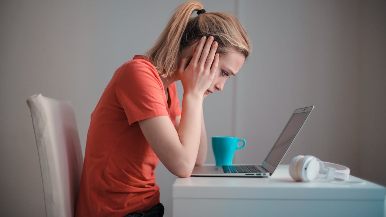 A woman sitting alone by a window with a cup of coffee, looking thoughtfully at her phone in soft morning light.