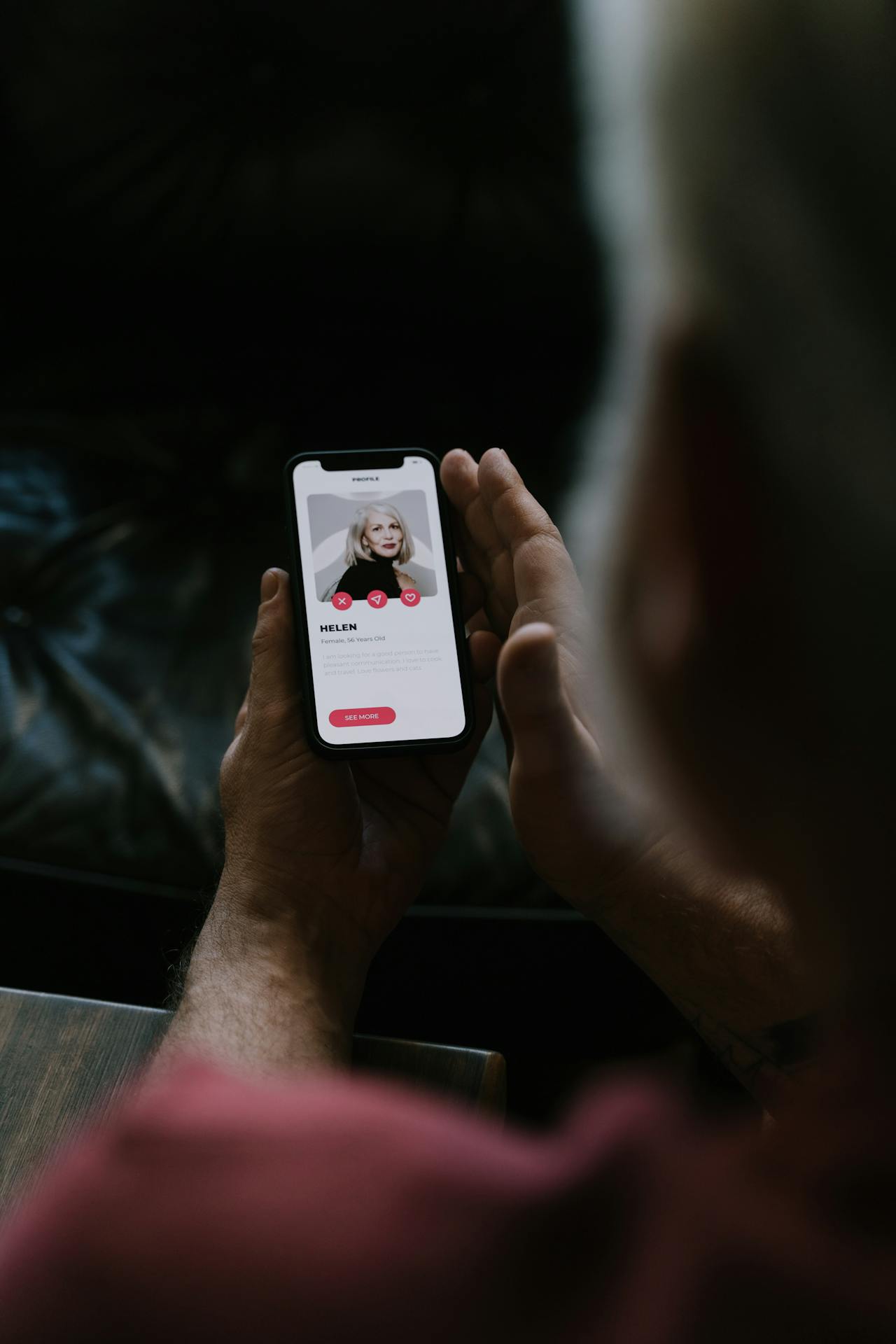 Hands holding a smartphone in a warmly lit cafe, a dating app profile visible on screen.