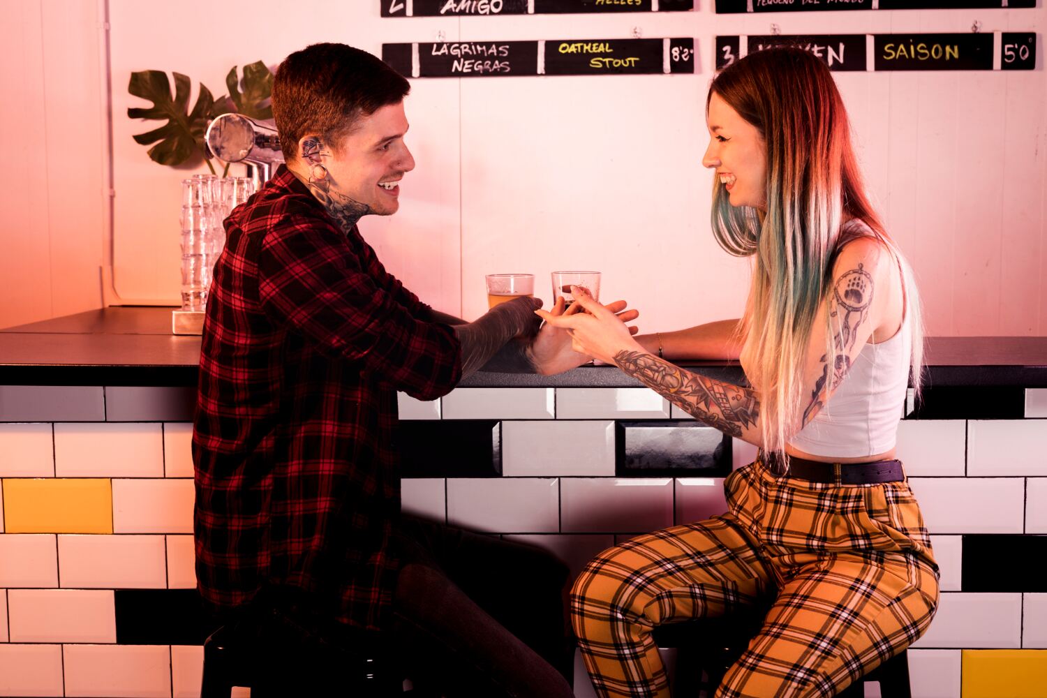 A couple at a bar clinking glasses, smiling at each other under warm pink lighting.