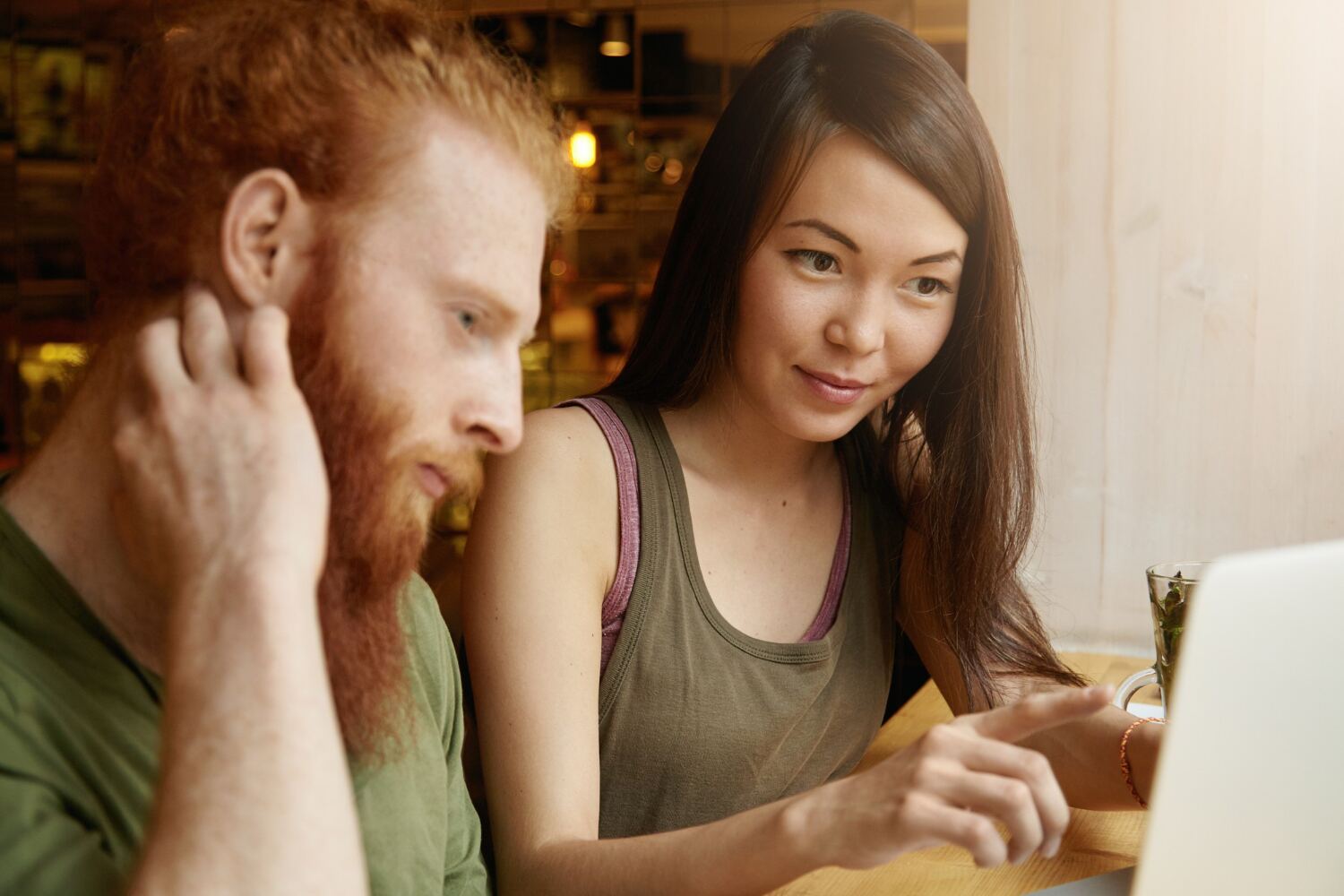A man and a woman sitting together at a cafe table looking intently at a laptop screen.